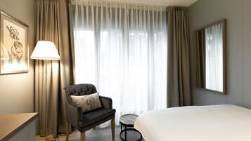 Una habitación de hotel con una cama, una silla, una lámpara, una mesita y una ventana con cortinas.