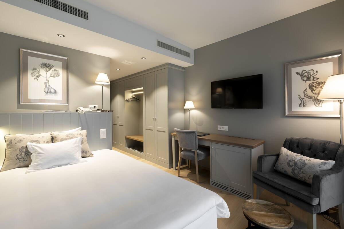 Ein Hotelzimmer mit einem großen Bett, einem Schreibtisch, einem Sessel, einem Fernseher und Bildern an den Wänden.
