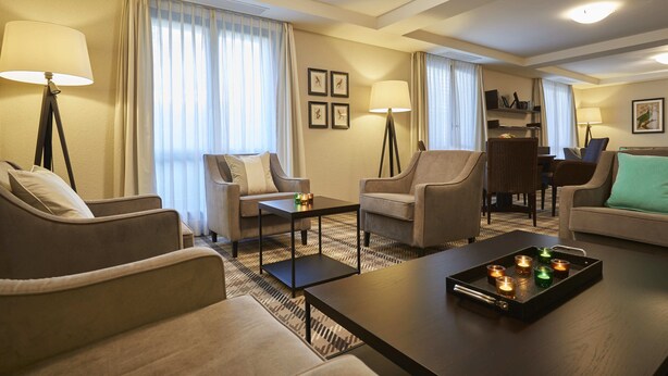 A hotel room with a sofa, armchairs, a coffee table with candles, and a dining area with chairs and a table. - Ascovilla (Ascona)