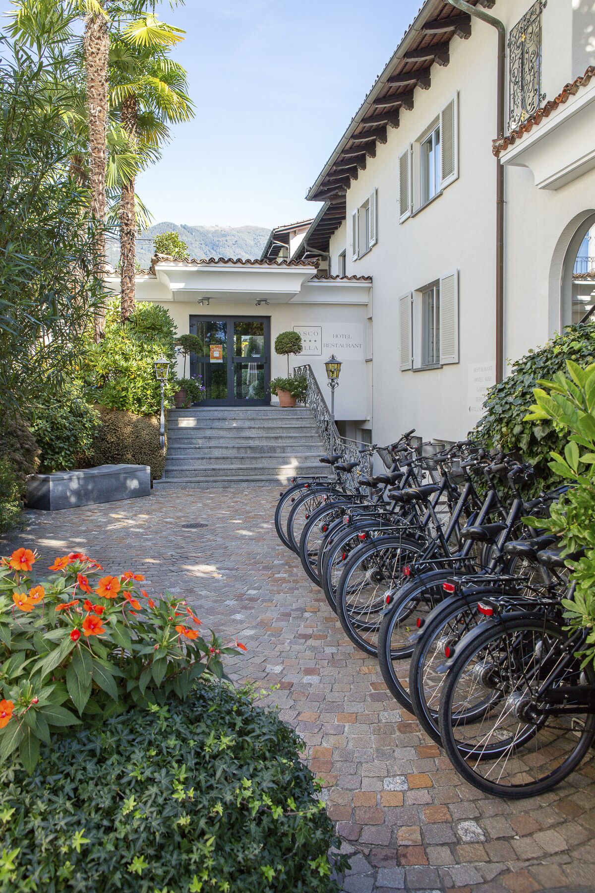 L’entrée d’un hôtel, avec un chemin pavé, une rangée de vélos et une vue sur les montagnes en arrière-plan.