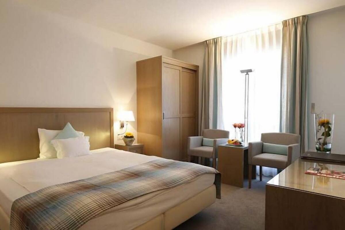 Ein Hotelzimmer mit einem großen Bett, einem Schreibtisch, zwei Stühlen, einem Kleiderschrank und einer Stehlampe.