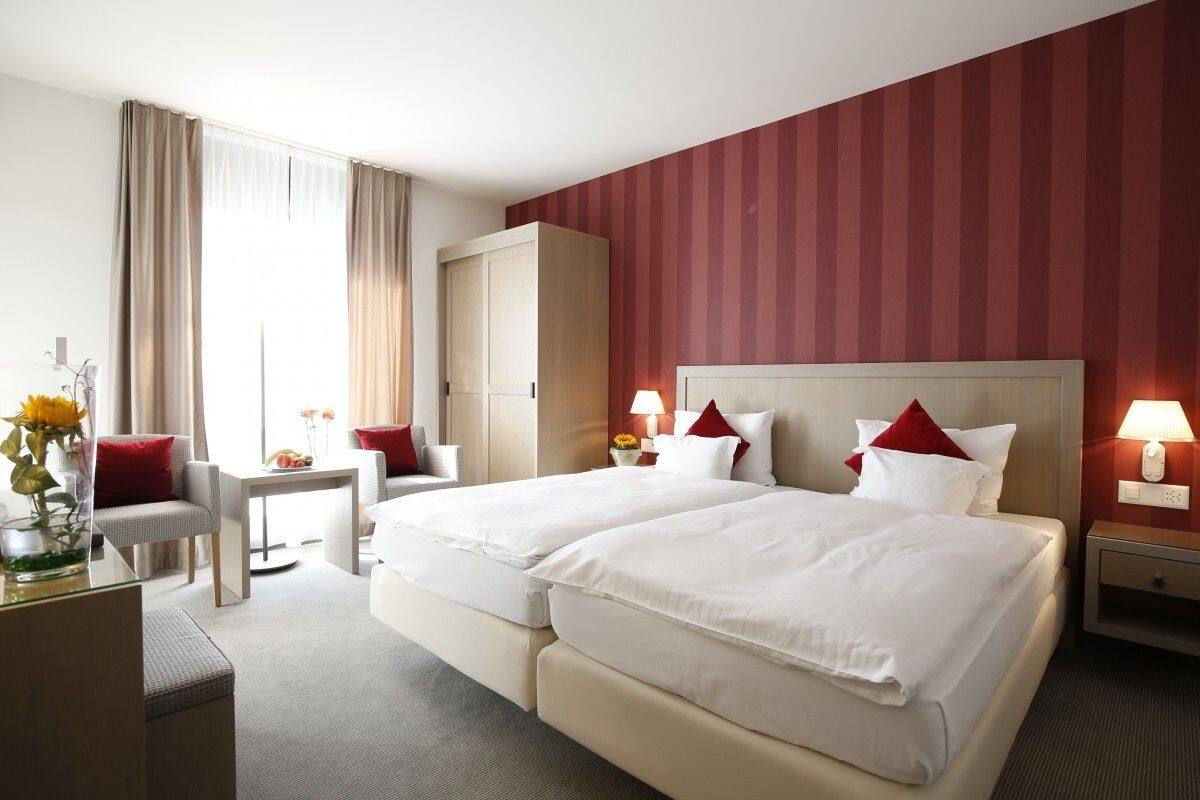 Ein Hotelzimmer mit zwei Betten, einem Schreibtisch, einem Stuhl, einem Kleiderschrank und einem Nachttisch mit Lampen.