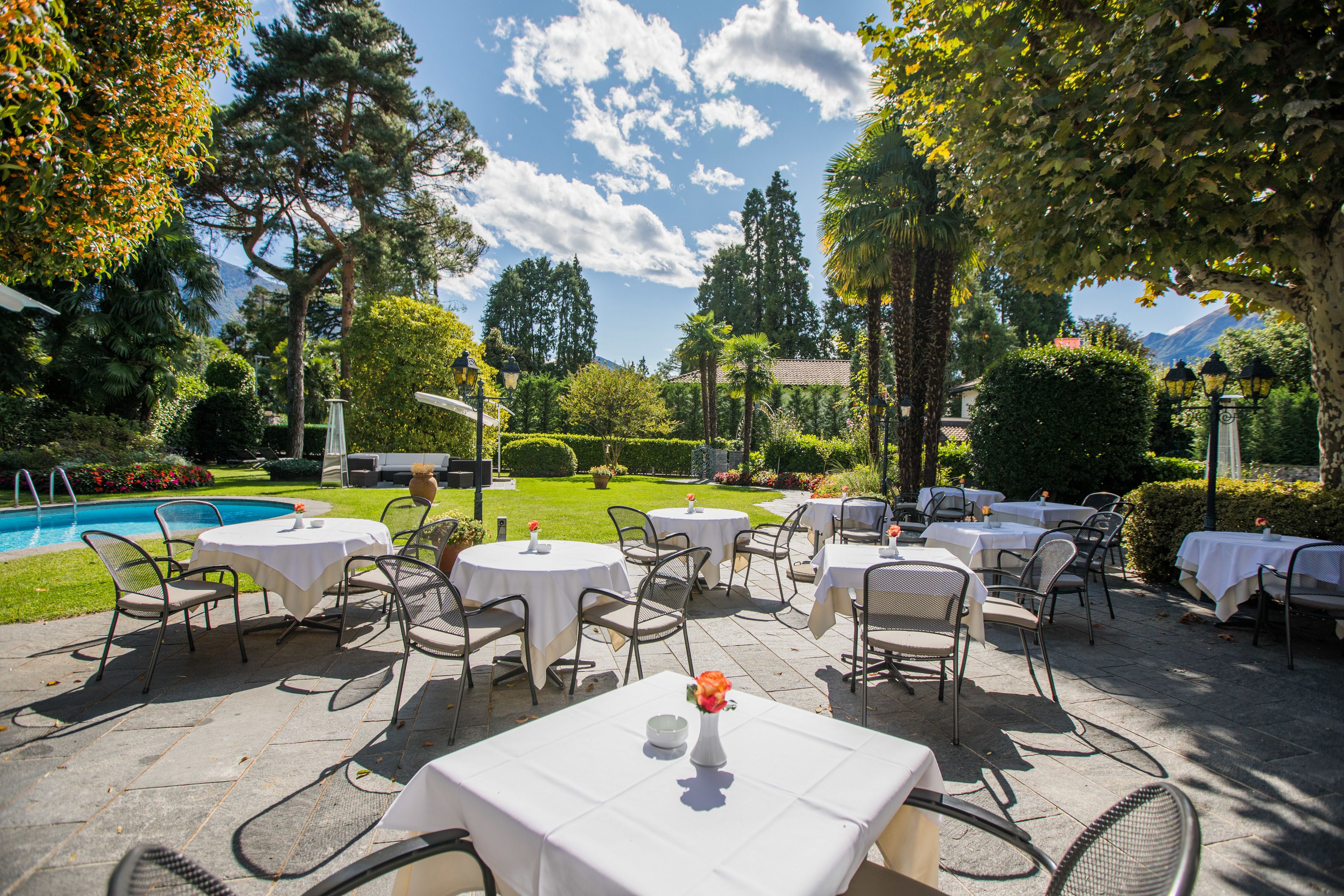 An outdoor patio with round tables and chairs, a pool, and a mountainous backdrop.