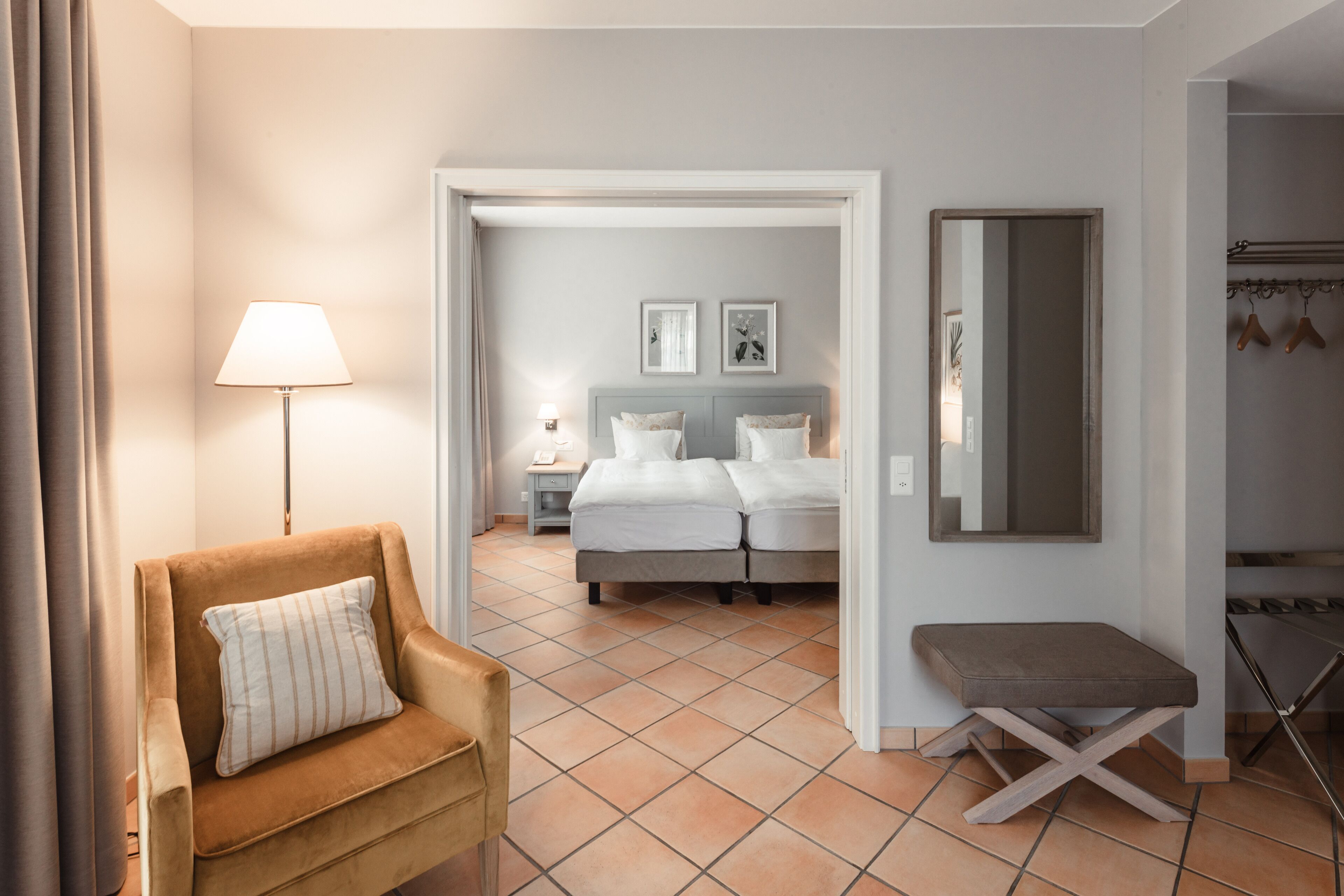 A hotel room with a bed, a chair, a bedside table, a lamp, and a mirror.