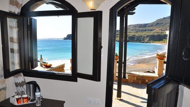 Quarto com vista para a praia e o mar através de uma porta aberta.