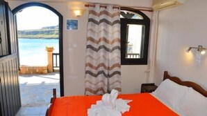 Um quarto com cama, janela, cortina e vista para o mar.