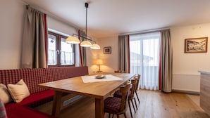 A dining area with a wooden table, red checkered sofa, and red upholstered chairs. - Haus Margareth (Wagrain)