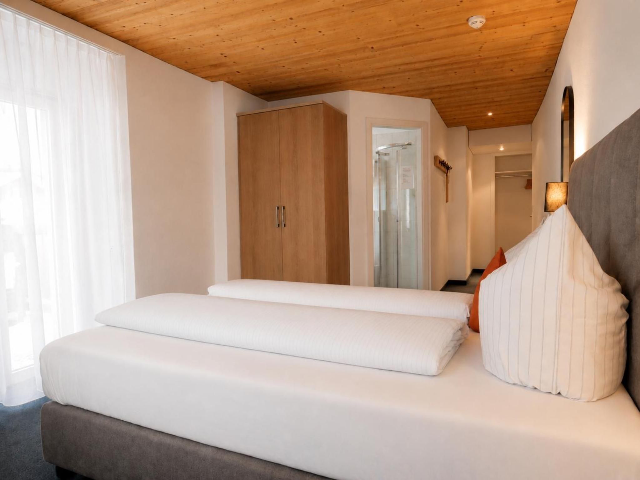 Een slaapkamer met een houten plafond, een bed met wit beddengoed, een kledingkast en een spiegel.