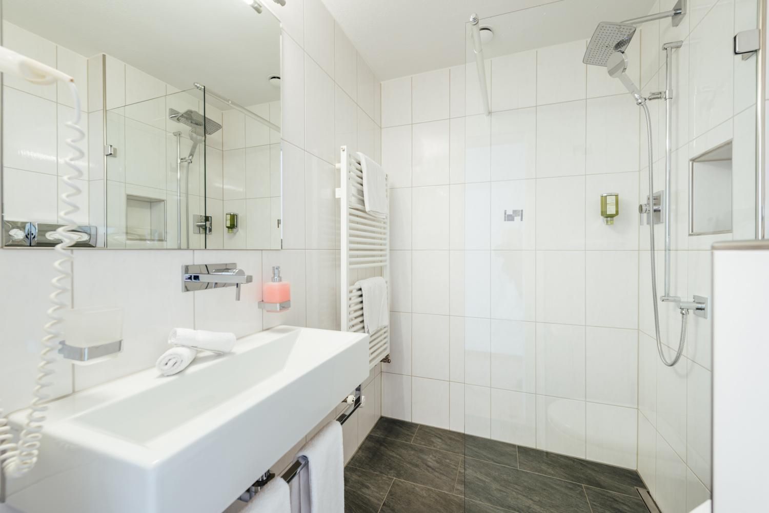 Une salle de bain moderne avec une douche à parois de verre, un lavabo blanc et un porte-serviettes.