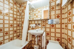 Un baño con ducha, lavabo e inodoro, con azulejos estampados y un espejo.