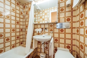 Un baño con ducha, lavabo e inodoro, con azulejos estampados y un espejo.