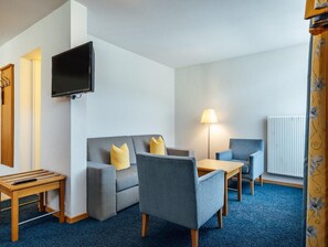 A hotel room with a sofa, two armchairs, a small table, a TV mounted on the wall, a lamp, and a radiator.