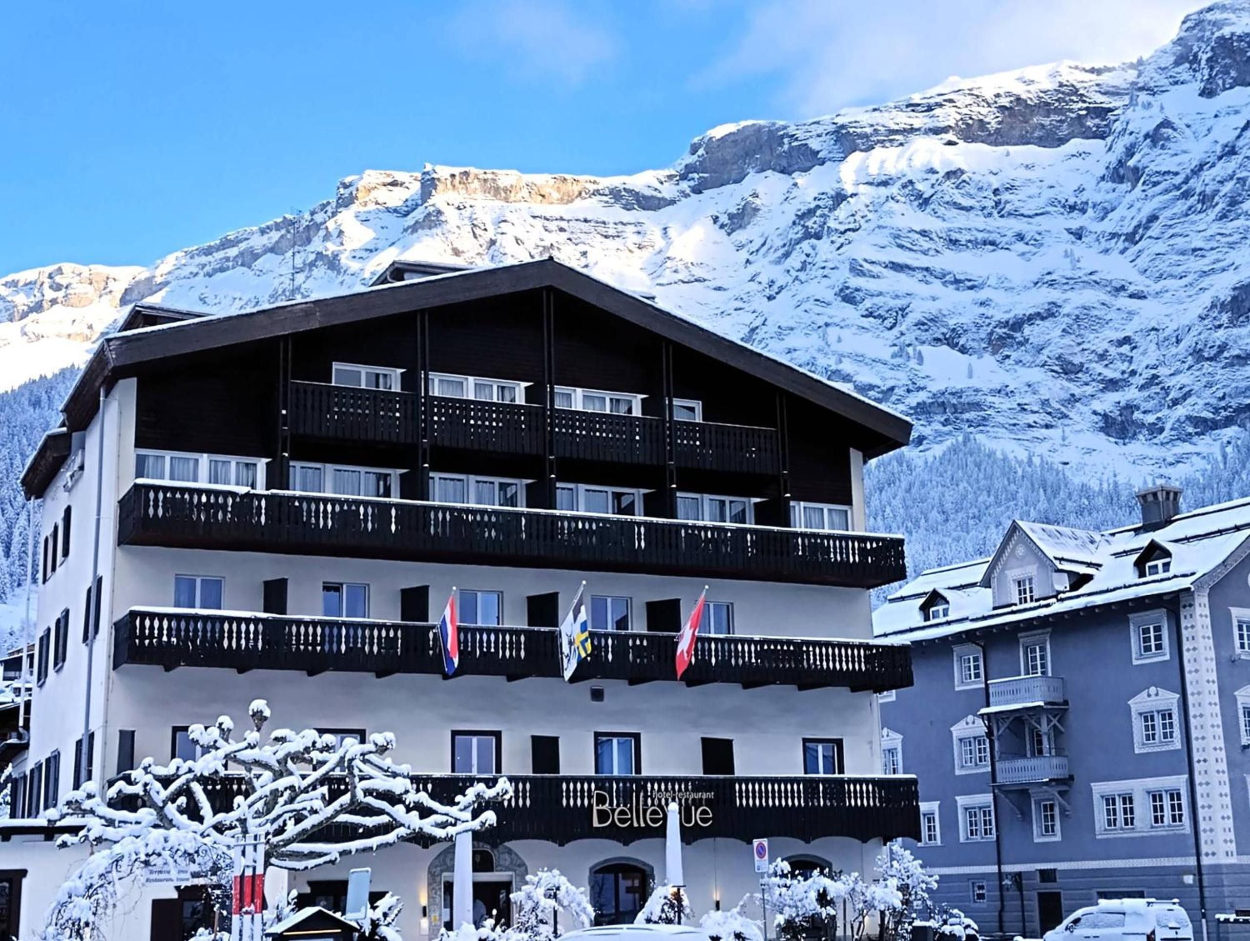 Un hôtel à plusieurs étages, doté de balcons, de drapeaux et surplombant un paysage montagneux.