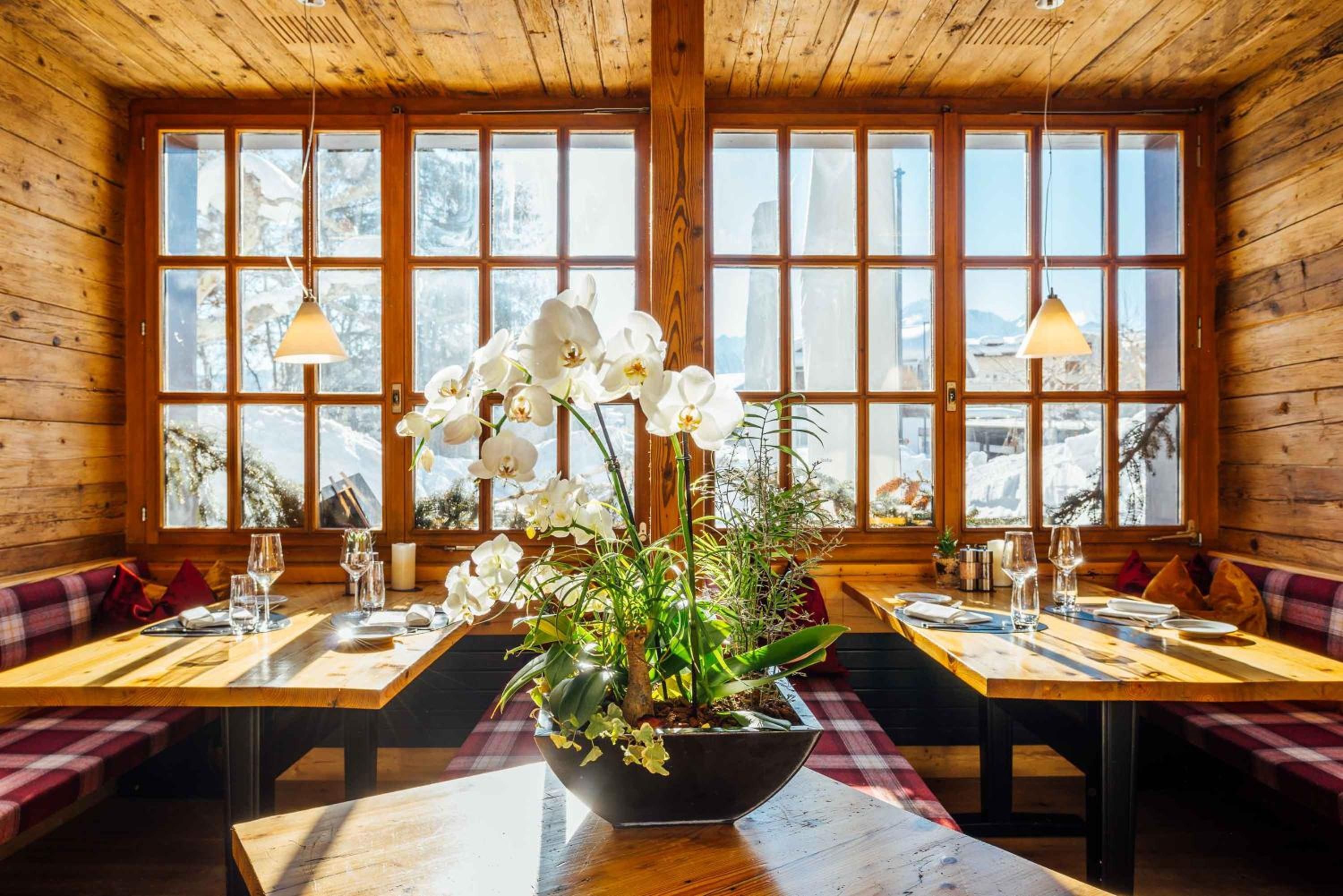 Un restaurant au décor intérieur en bois, doté de grandes fenêtres et d’une table agrémentée d’un arrangement floral.