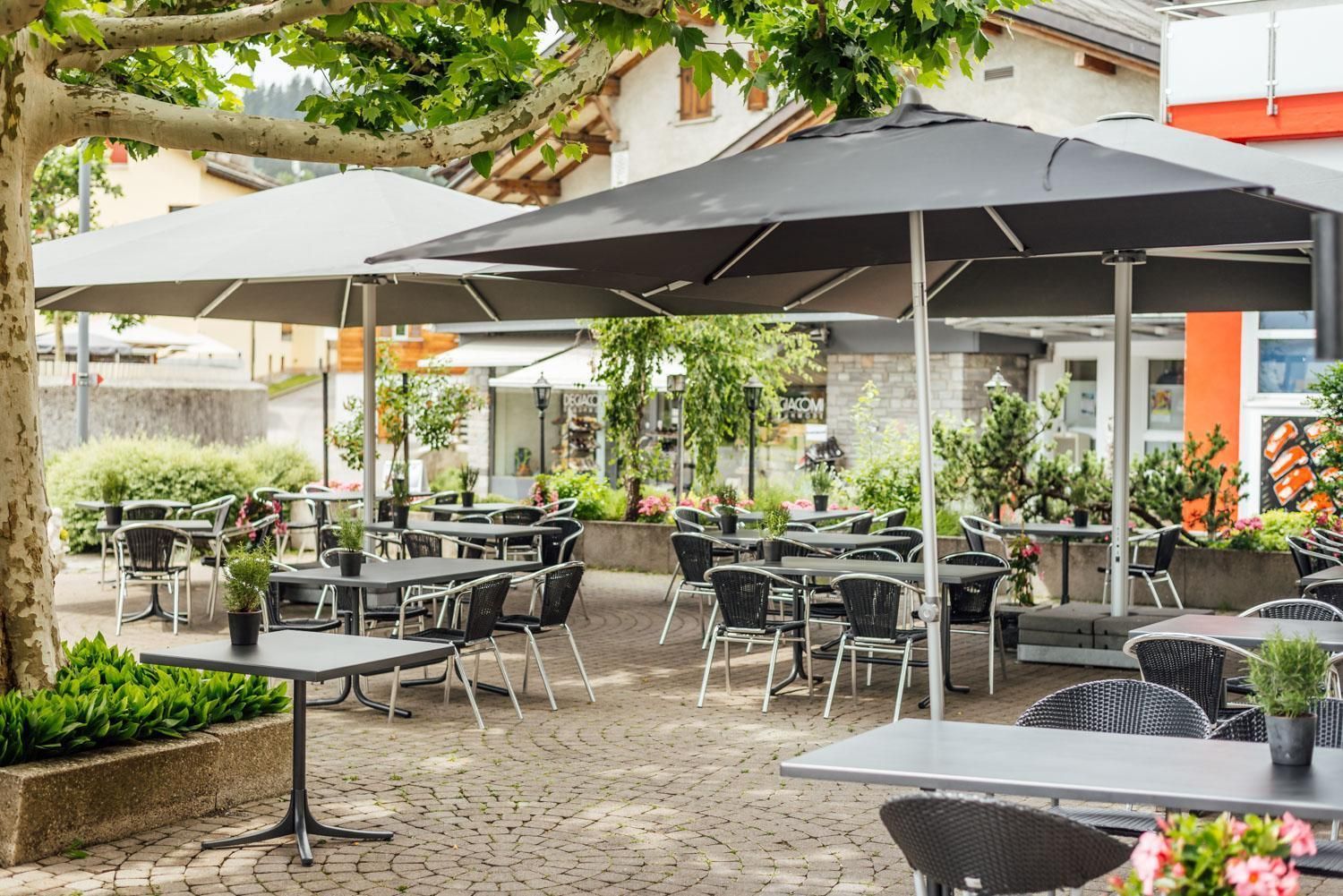 Un café al aire libre con mesas, sillas, sombrillas y plantas en macetas.