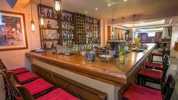 A bar area with a wooden counter, red cushioned bar stools, and shelves stocked with bottles.