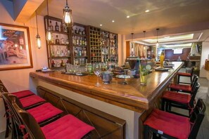 A bar area with a wooden counter, red cushioned bar stools, and shelves stocked with bottles. - Thalassies Nouveau (Thasos)
