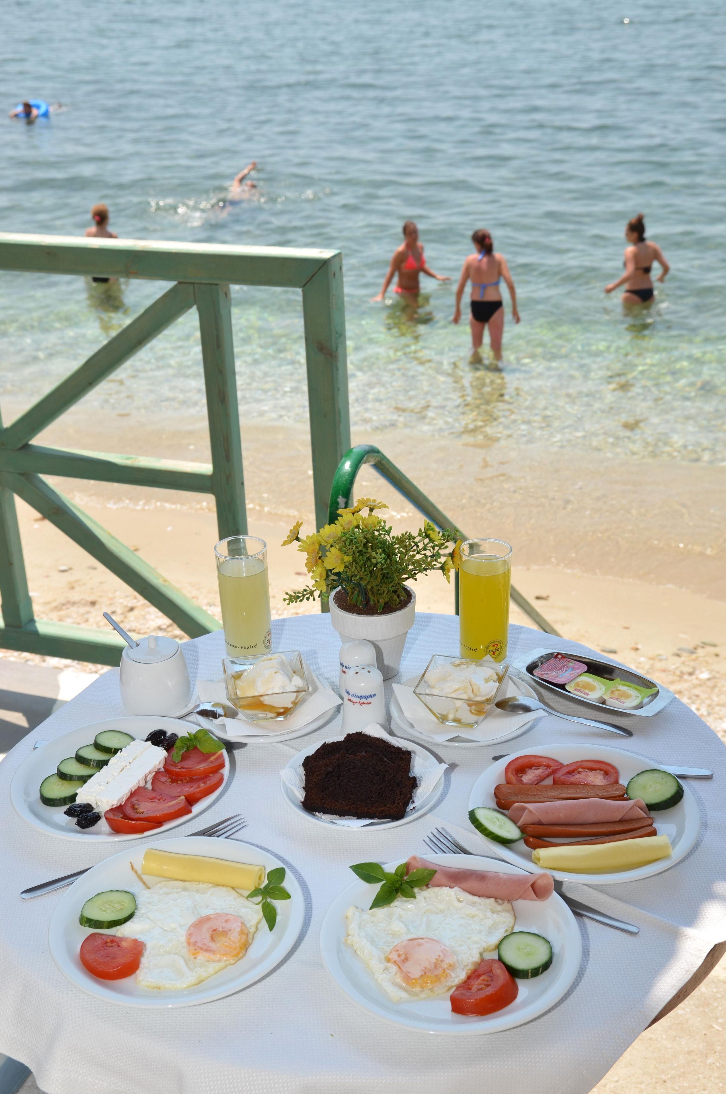 A table with breakfast items and drinks on a beach with people in the water.