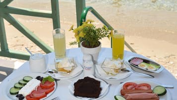 A table with breakfast items and drinks on a beach with people in the water.