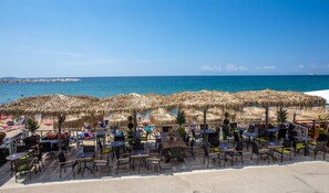 Ein Strandcafé mit Außenbestuhlung und Sonnenschirmen mit Blick aufs Meer.