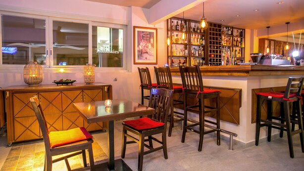 A bar area with a wooden counter, multiple chairs with red cushions, and a shelf of liquor bottles. - Thalassies Nouveau (Thasos)
