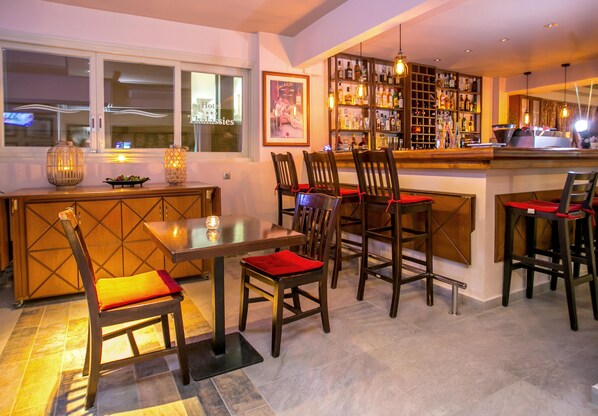 Eine Bar mit einer Holztheke, mehreren Sesseln mit roten Kissen und einer Flaschenregal.