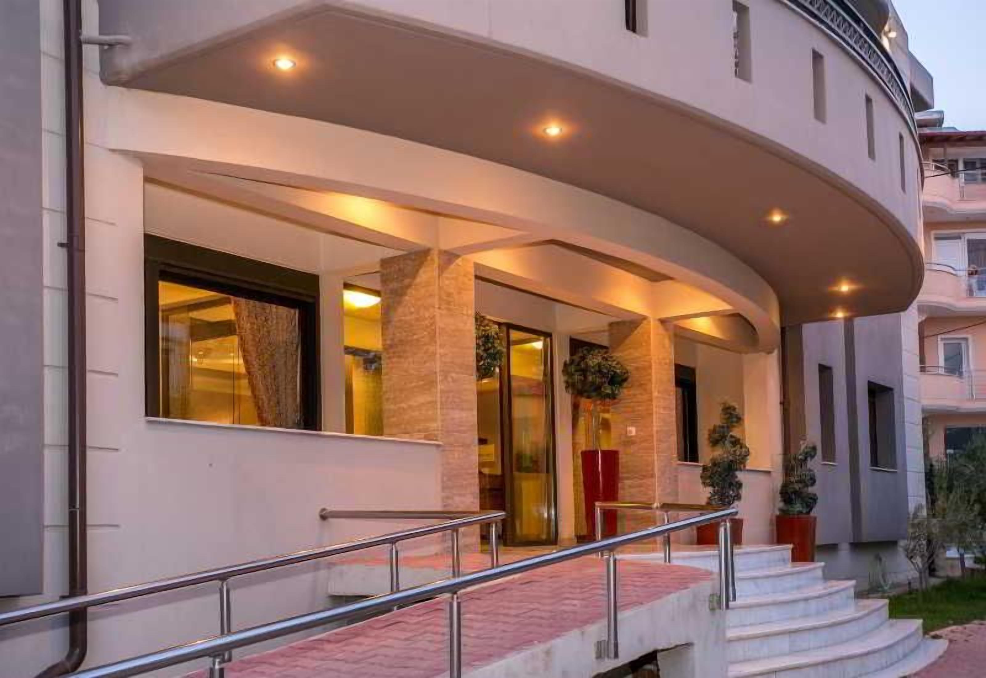 A hotel entrance with a curved facade, a staircase leading to the entrance, and potted plants.