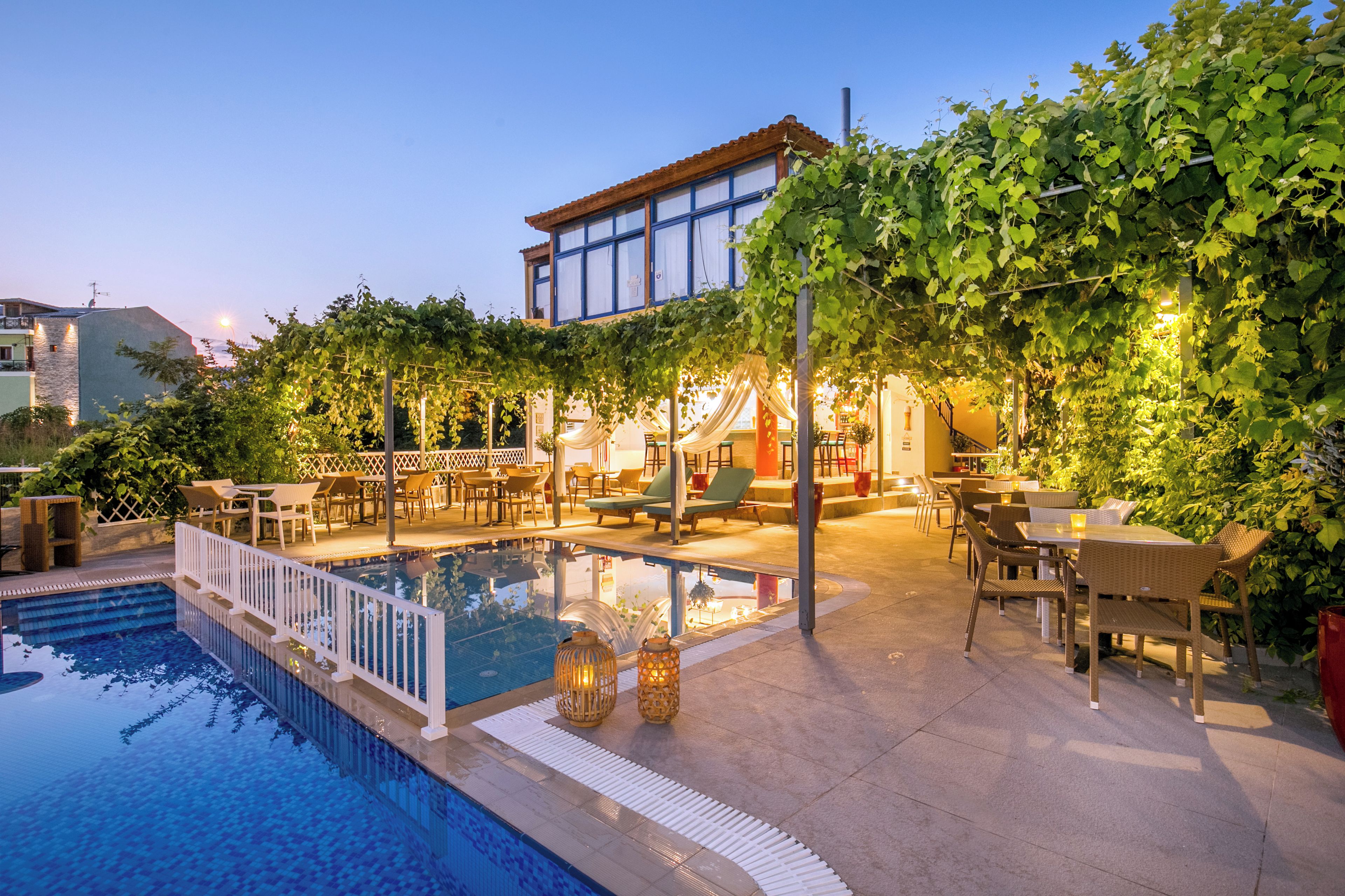 A pool area with a pergola, outdoor seating, and a building with large windows.