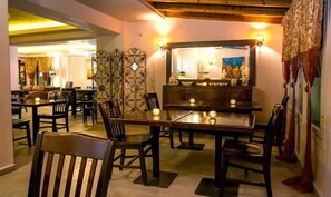 A dining area with wooden tables and chairs, a decorative metal partition, and a mirror above the counter. - Thalassies (Thasos)