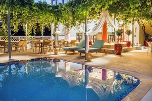 An outdoor pool area with lounge chairs, a table, and a pergola with draped fabric. - Thalassies (Thasos)