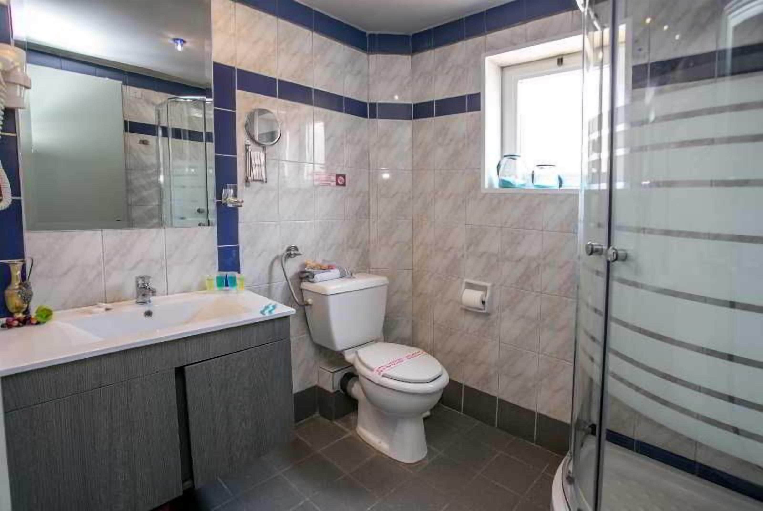 Un baño con inodoro blanco, lavamanos con espejo y zona de ducha.