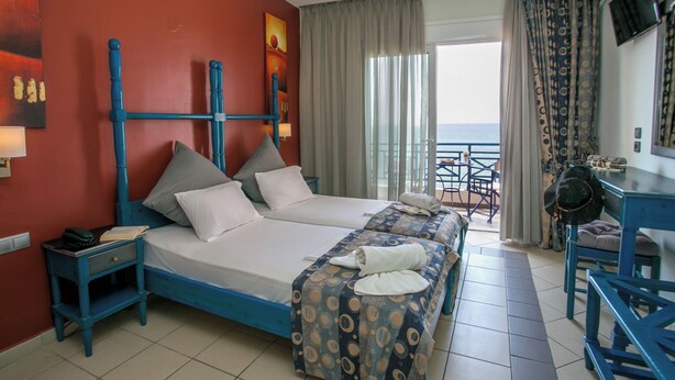 Een hotelkamer met twee bedden, een bureau, een stoel en een balkon met uitzicht.