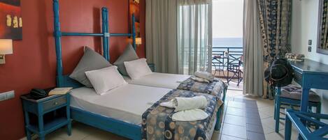 A hotel room with two beds, a desk, a chair, and a balcony with a view.
