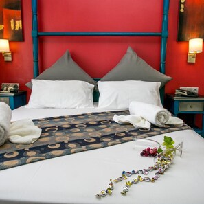 A hotel room with a red wall, two grey pillows, a white bedspread, and a blue patterned throw. - Thalassies (Thasos)