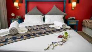 Een hotelkamer met een rode accentmuur, een bed met witte lakens, twee kussens, een geborduurde spreideken en twee nachtkastjes met lampen.