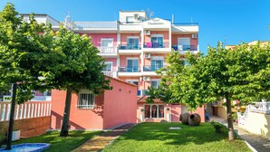 A hotel with a pink facade, multiple balconies, and a well-maintained garden with trees and a small fountain. - Thalassies (Thasos)