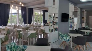 Ein Restaurant mit mehreren Tischen, Stühlen, einem Bücherregal und einem Fernseher an der Wand.