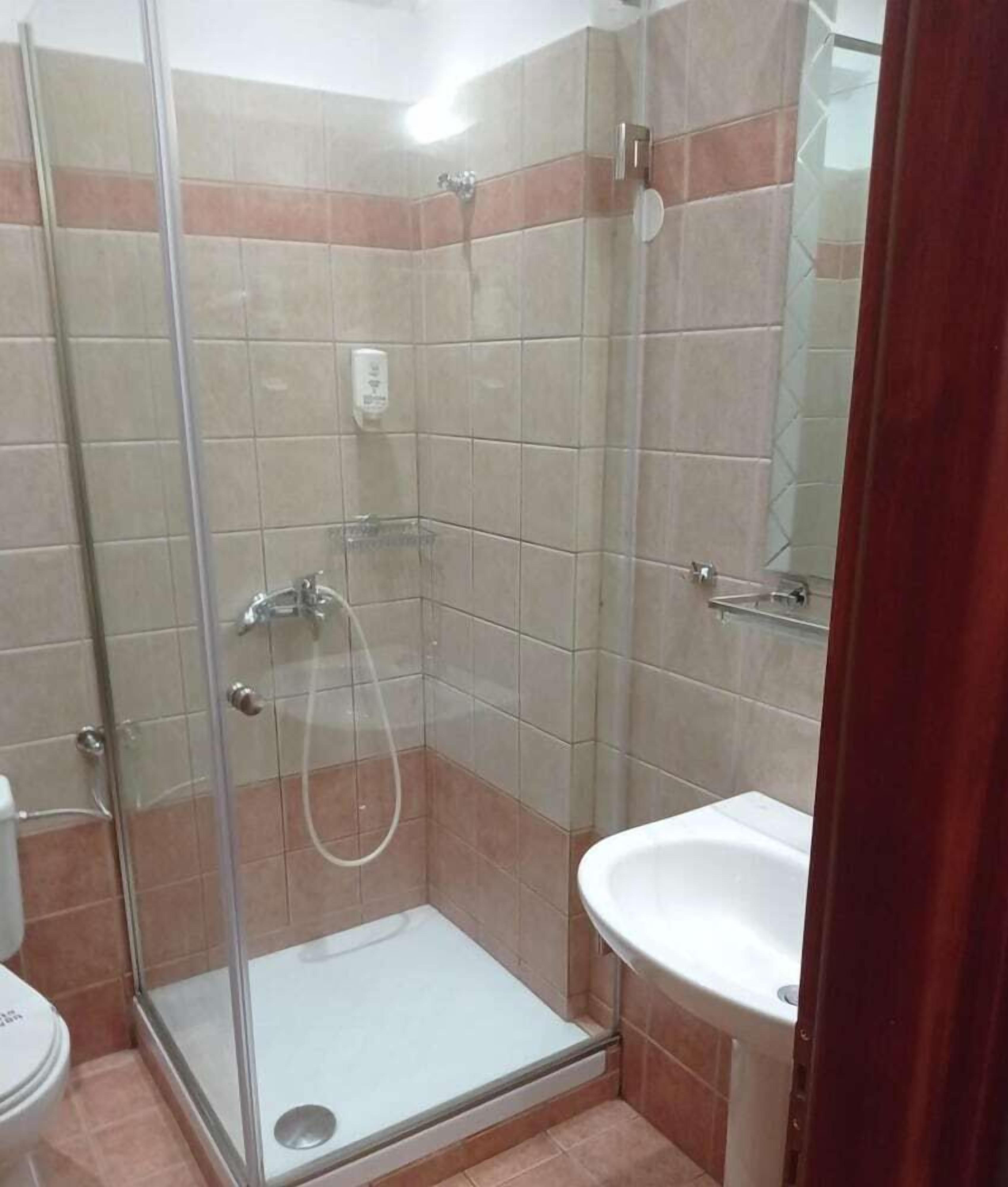 A bathroom with a glass shower enclosure, a white sink, and tiled walls.