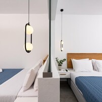 Una habitación de hotel moderna con dos camas, una mesita de noche, una planta en maceta y luces colgantes.