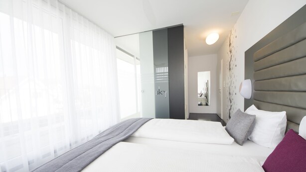 A hotel room with a large bed, a bedside table, a mirror, and a view of the outdoors. - Sky Design Motel (Oberriet)
