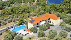 Ein Luftbild eines Anwesens an der Küste mit Swimmingpool, überdachter Außenlounge und einem Gebäude mit rotem Dach.
