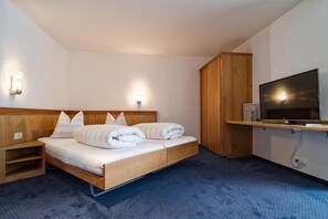 A hotel room with a single bed, wooden headboard, bedside tables, a wardrobe, a television, and a wall-mounted light fixture.