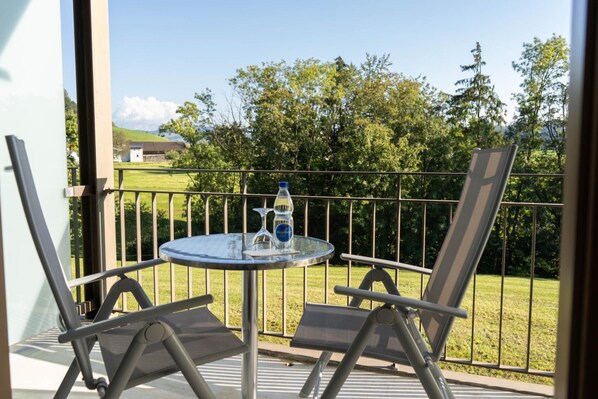 A balcony with a round table, two chairs, a bottle, and a glass.