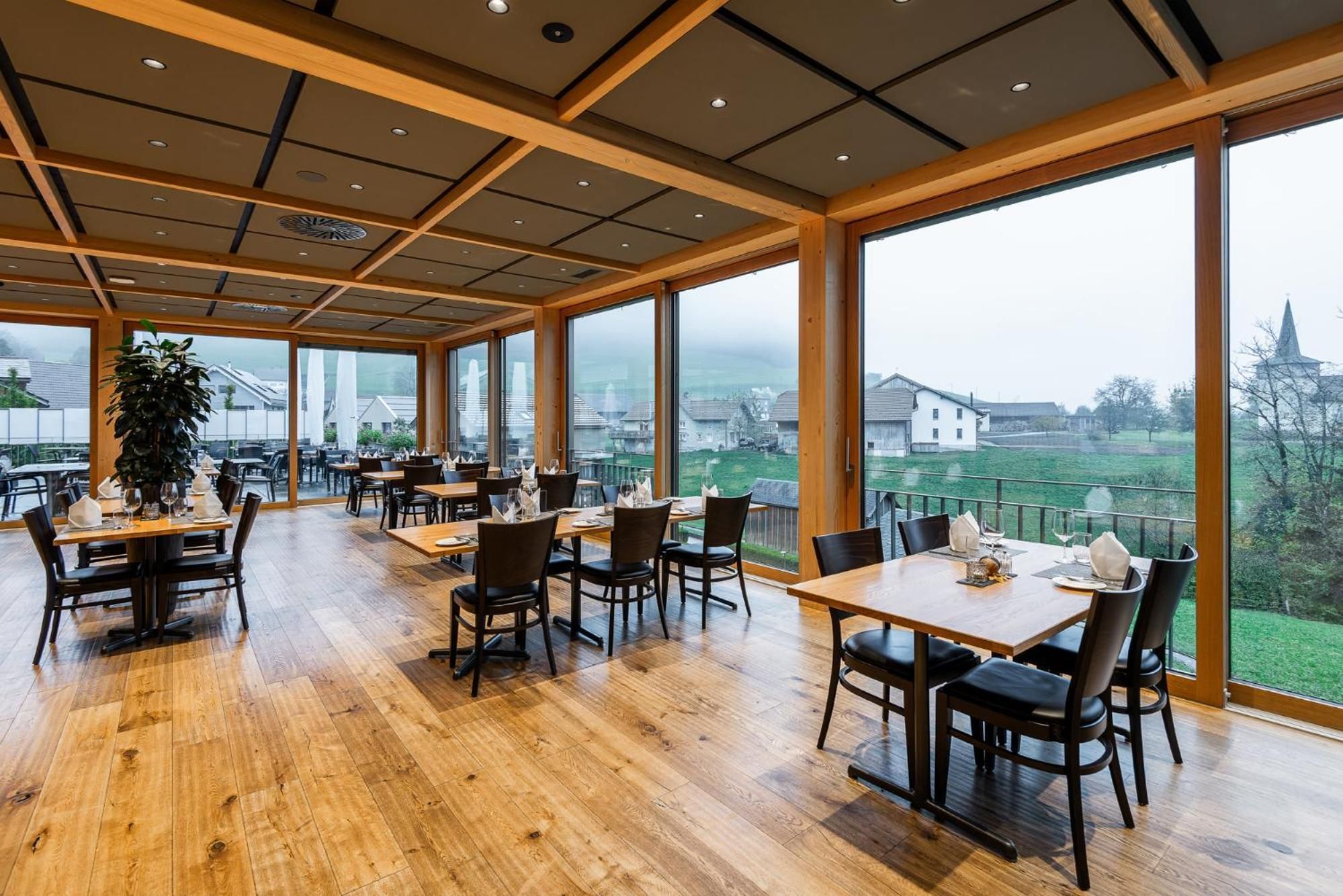 Un restaurante con suelo de madera y ventanas amplias que ofrecen vistas al campo.