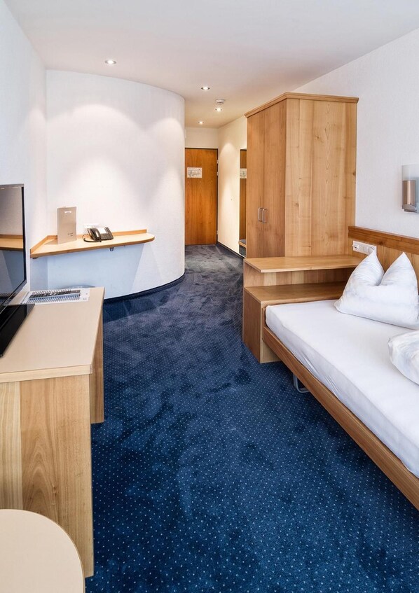 A hotel room with a desk, a bed, a wardrobe, and a bathroom door.