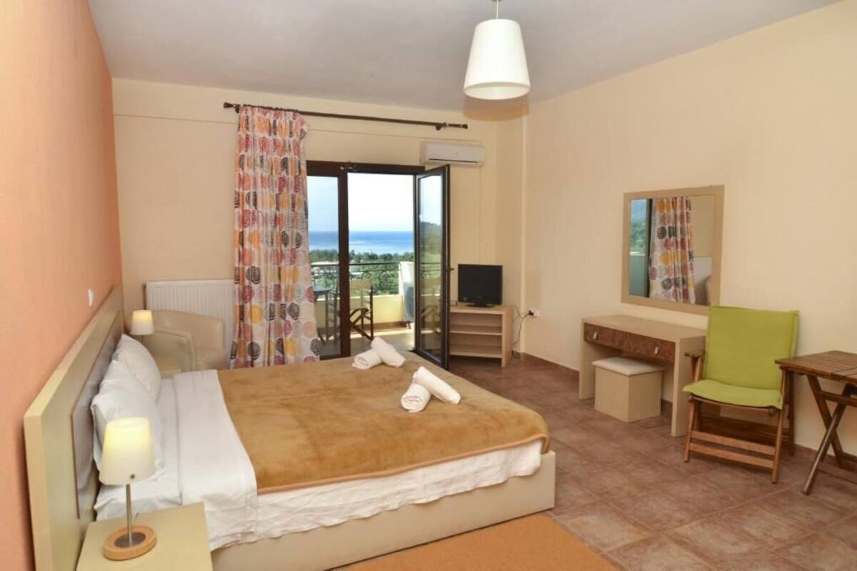 A hotel room with a bed, a desk, a chair, a TV, and a balcony with a view.