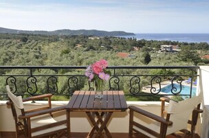 Un balcón con mesa y sillas, un jarrón con flores y vistas a un paisaje costero con piscina.