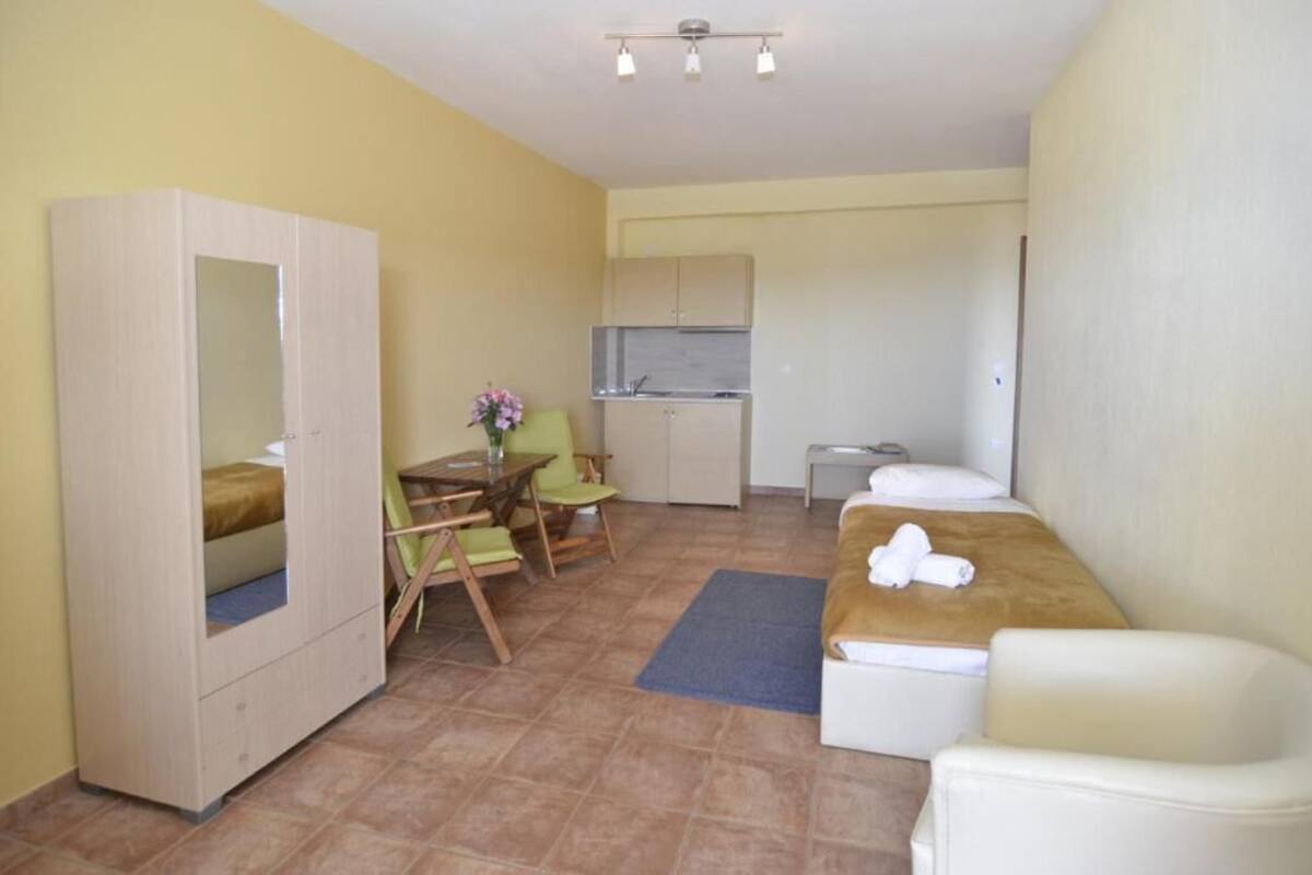 A compact room with a bed, a small kitchenette, a dining table with chairs, and a wardrobe.