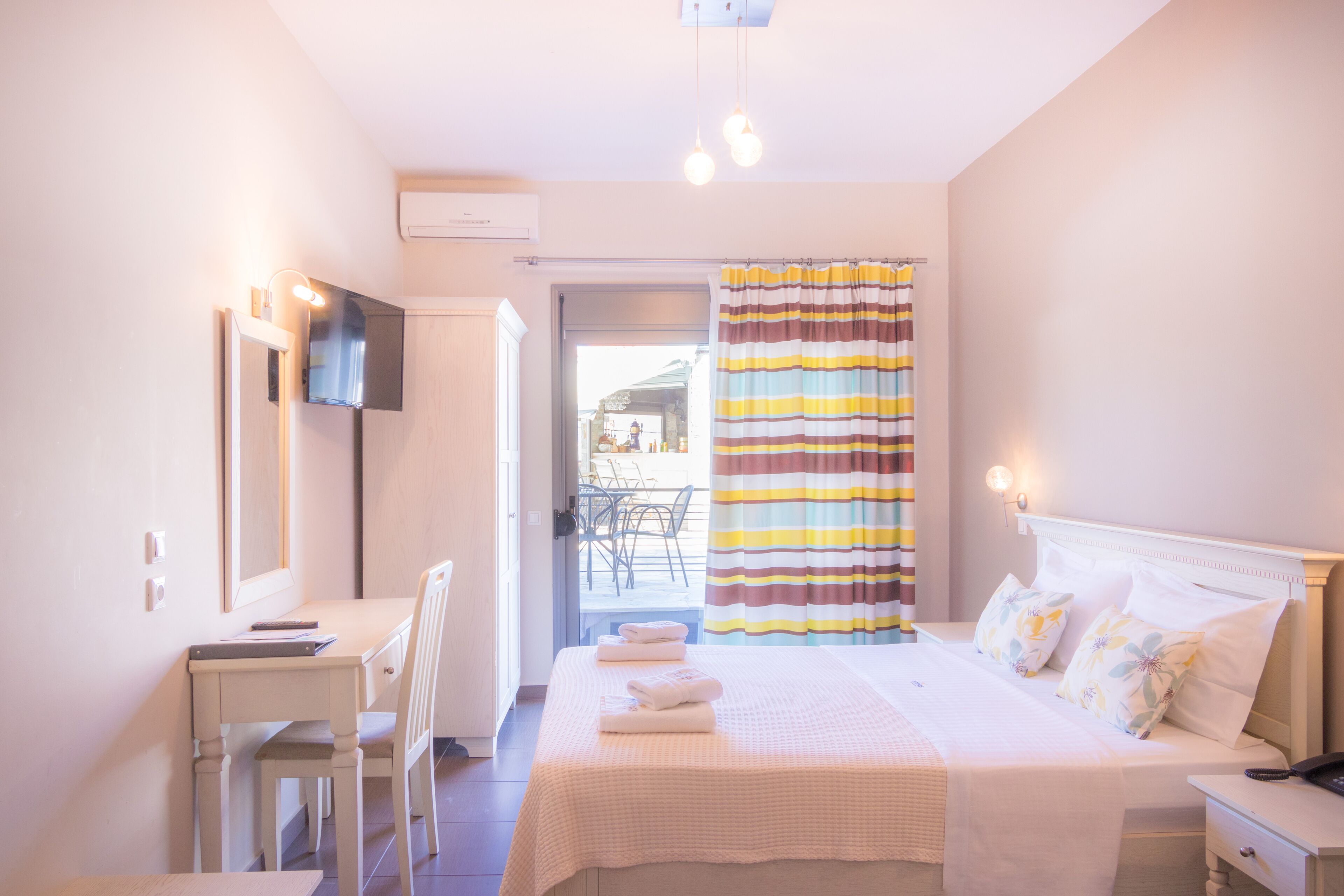 Habitación de hotel con cama, escritorio, silla, televisor montado en la pared y baño con cortina de ducha a rayas.