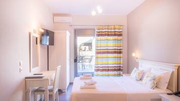 Habitación de hotel con cama, escritorio, silla, televisor montado en la pared y baño con cortina de ducha a rayas.